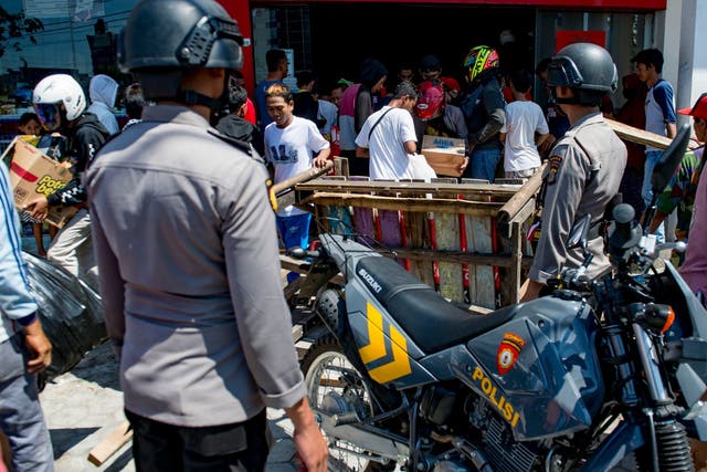 Police watch as people loot a convenience store in Palu, Sulawesi, on Sunday