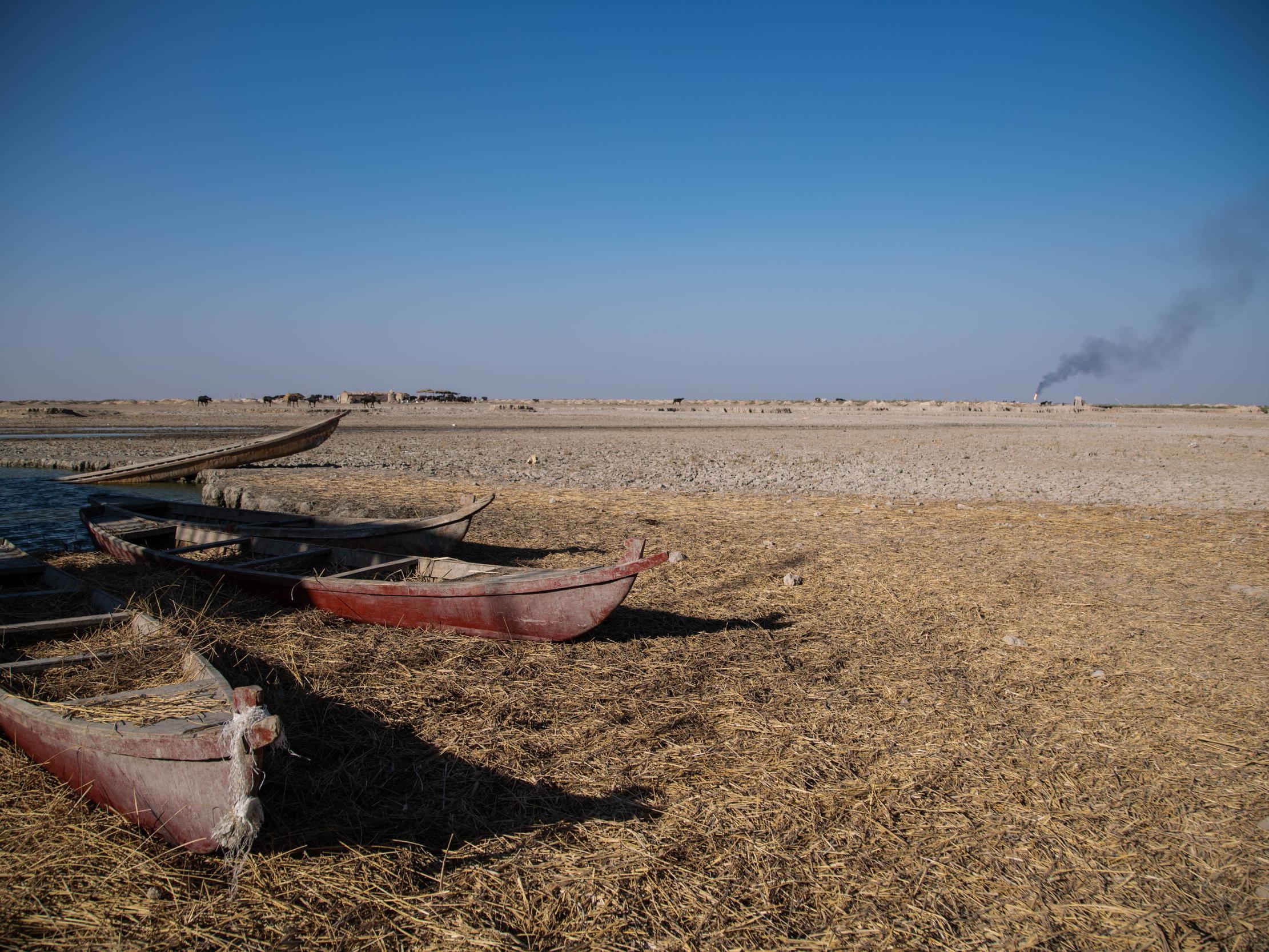 Smoke billows from an oil refinery in the background of a dried out marsh