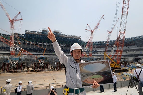 A staff member gestures while holding an image of the new National Stadium