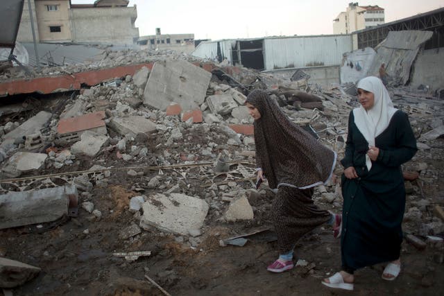 Palestinian women walk past buildings levelled by Israeli airstrikes in Gaza City on 27 October