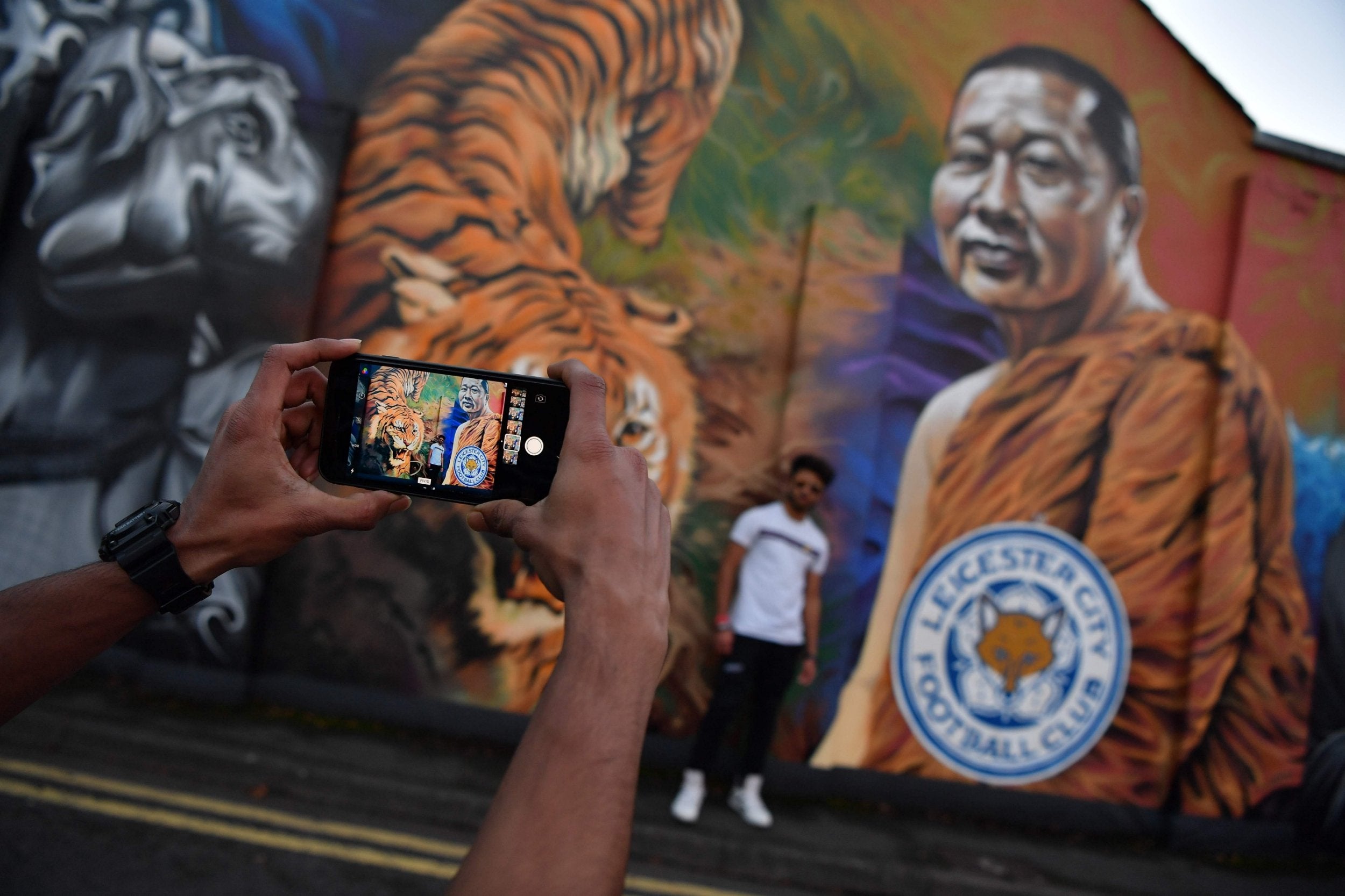 A man poses for a photograph against a mural showing Leicester City Football Club's Thai chairman Vichai Srivaddhanaprabha near De Montfort University in Leicester