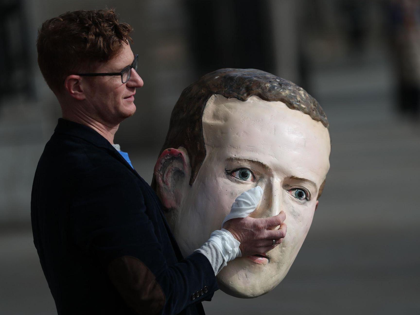A protestor from the pressure group Avaaz carries a papier mache head of Facebook founder Mark Zuckerberg outside Portcullis house