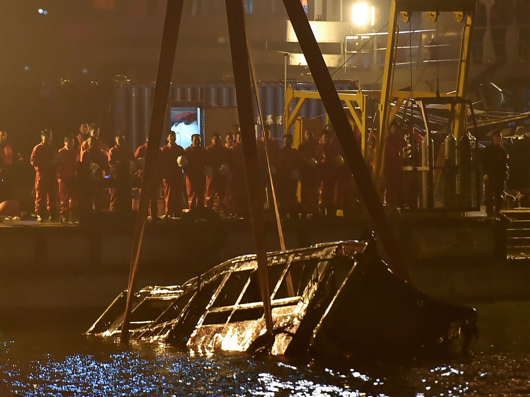 Rescuers watch as the bus is lifted out of the river by a floating crane