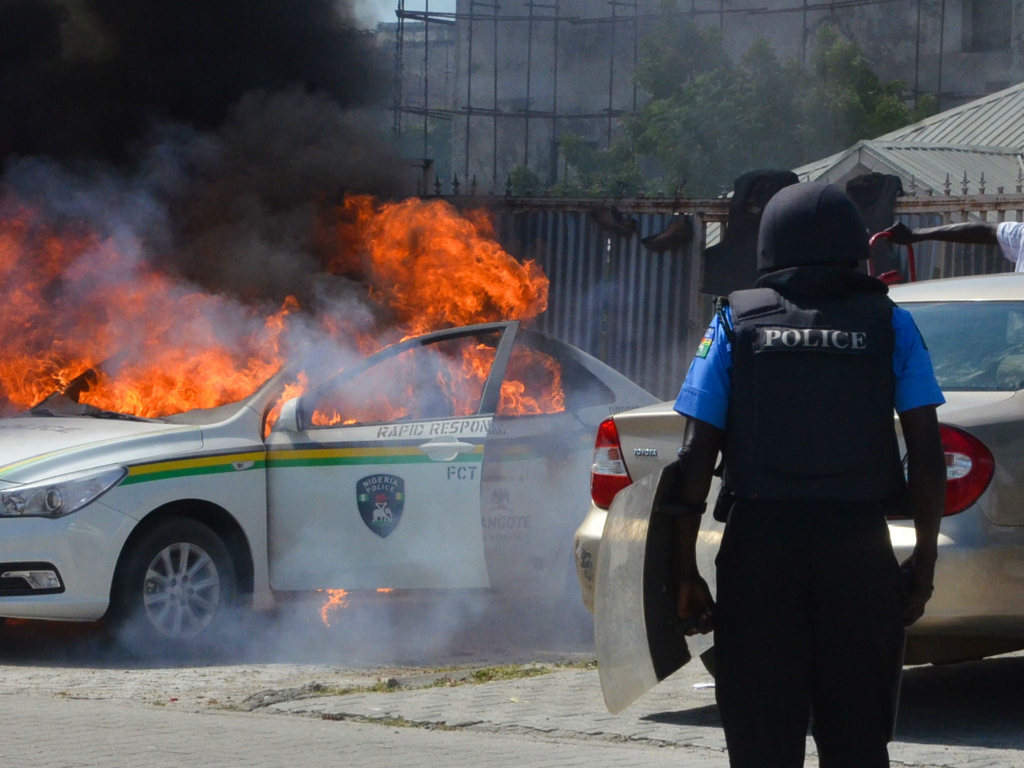 A Nigerian police officers watches a police vehicle as it goes up in flames following clashes with supporters of Islamic Movement of Nigeria (IMN) protesting against the imprisonment of their leade