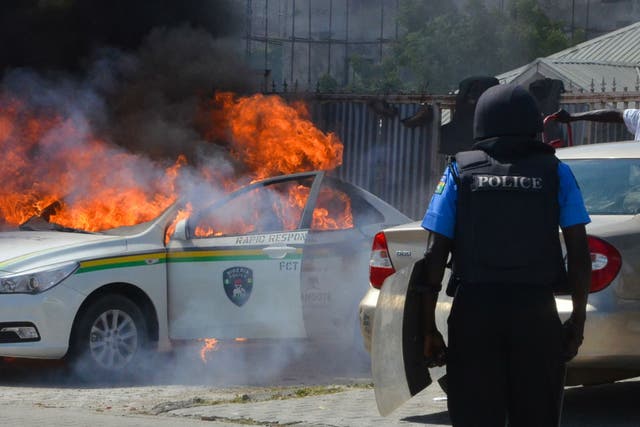 A Nigerian police officers watches a police vehicle as it goes up in flames following clashes with supporters of Islamic Movement of Nigeria (IMN) protesting against the imprisonment of their leade