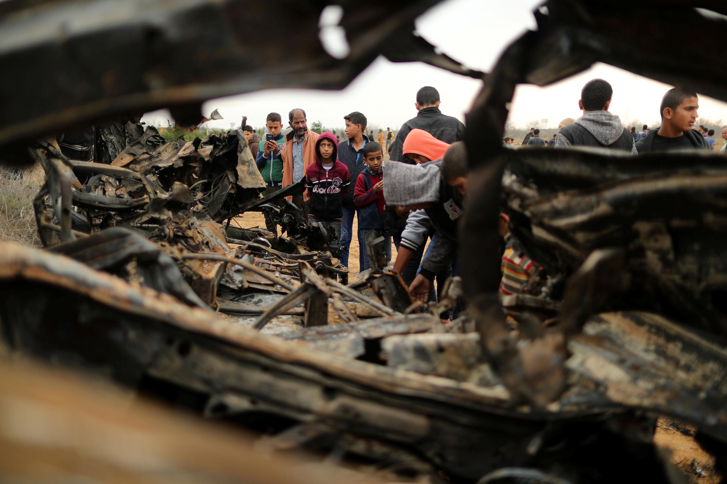 Palestinians gather around the remains of a vehicle that was destroyed in an Israeli air strike, in Khan Younis in the southern Gaza Strip
