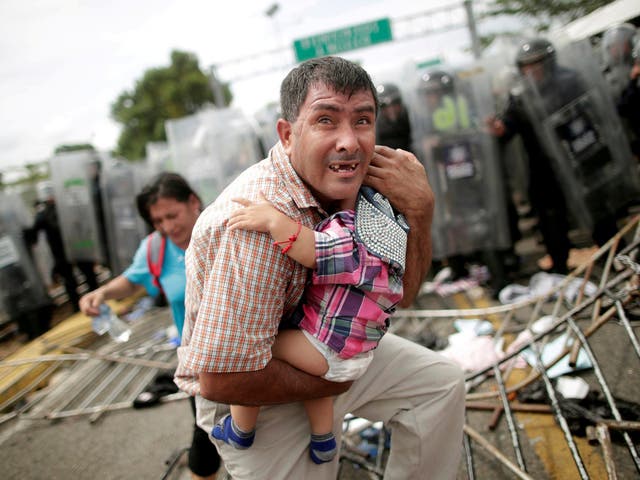 A Honduran man protects his child after migrants, part of a caravan trying to reach the US, stormed a border checkpoint in Guatemala