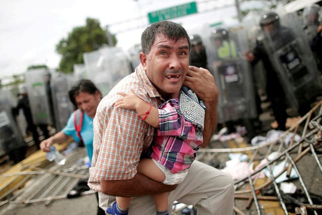 A Honduran man protects his child after migrants, part of a caravan trying to reach the US, stormed a border checkpoint in Guatemala