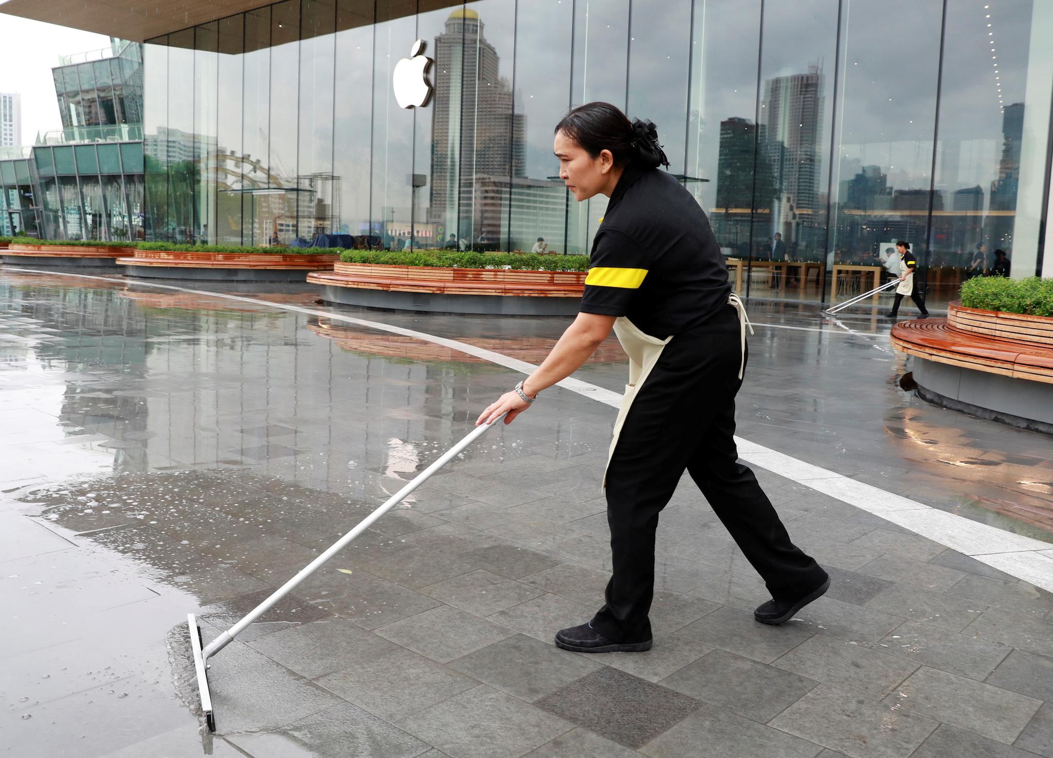 A woman cleans the wet floor near the Thailand's first flagship Apple store at Iconsiam shopping mall in Bangkok, Thailand