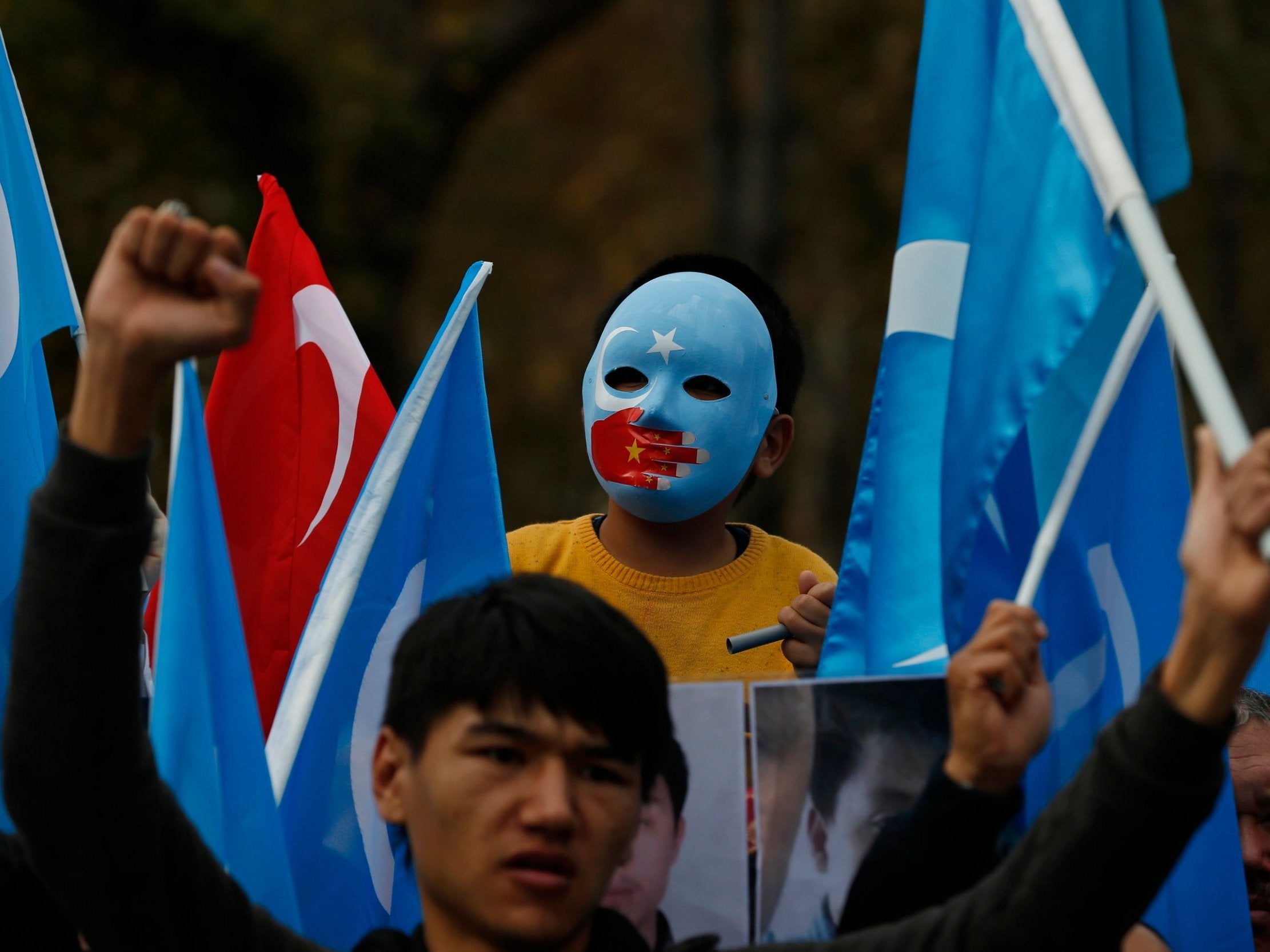 A child from the Uighur community living in Turkey wearing a mask in the colours of the flag what ethnic Uighurs call 'East Turkestan', with a painted hand with the colours of China's flag, participates in a protest in Istanbul