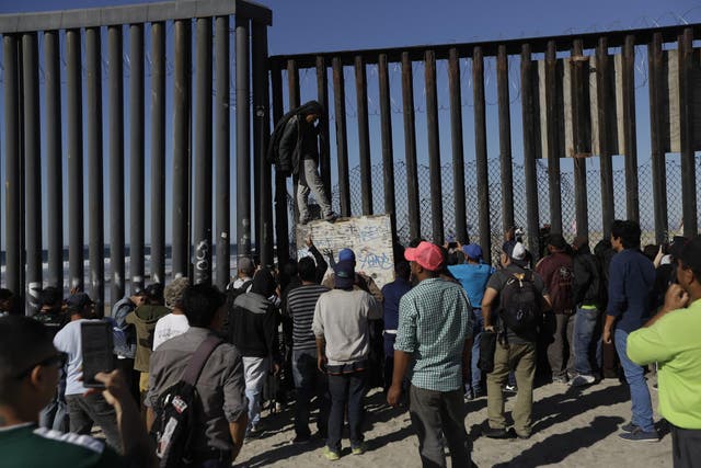 Central American migrants and others look on along the border structure, in Tijuana, Mexico Wednesday,