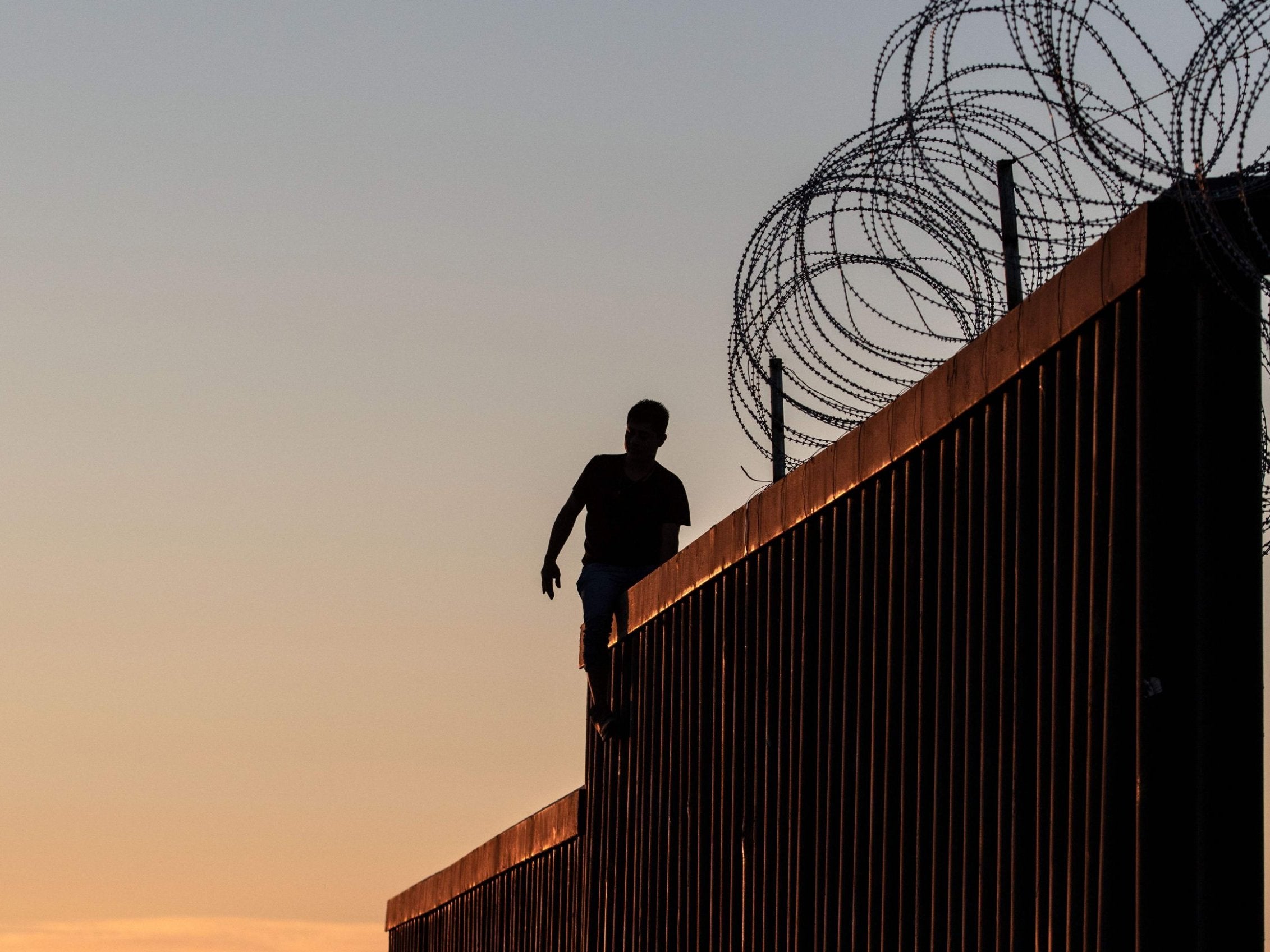 A man walks along the top of the fence separating the US and Mexico in California