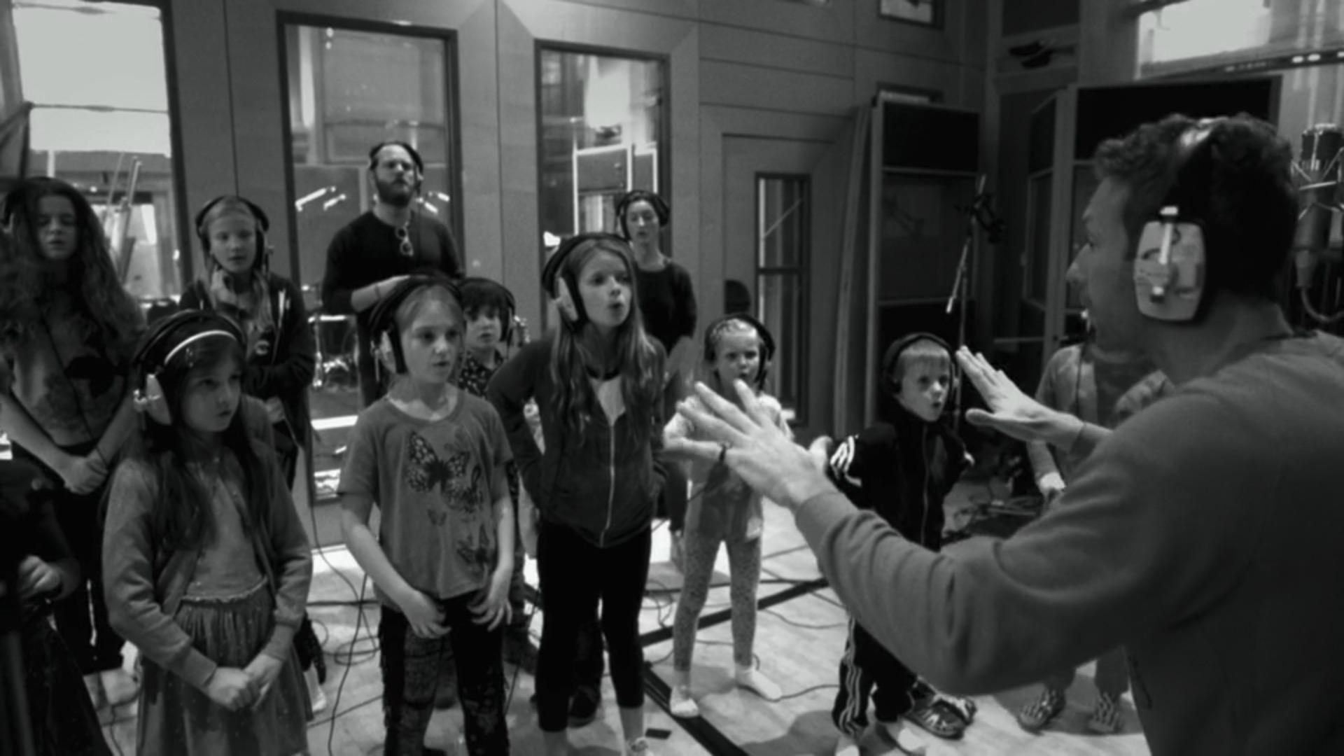 Chris Martin conducts a choir of children. The band's music has involved more choruses of voices in recent years