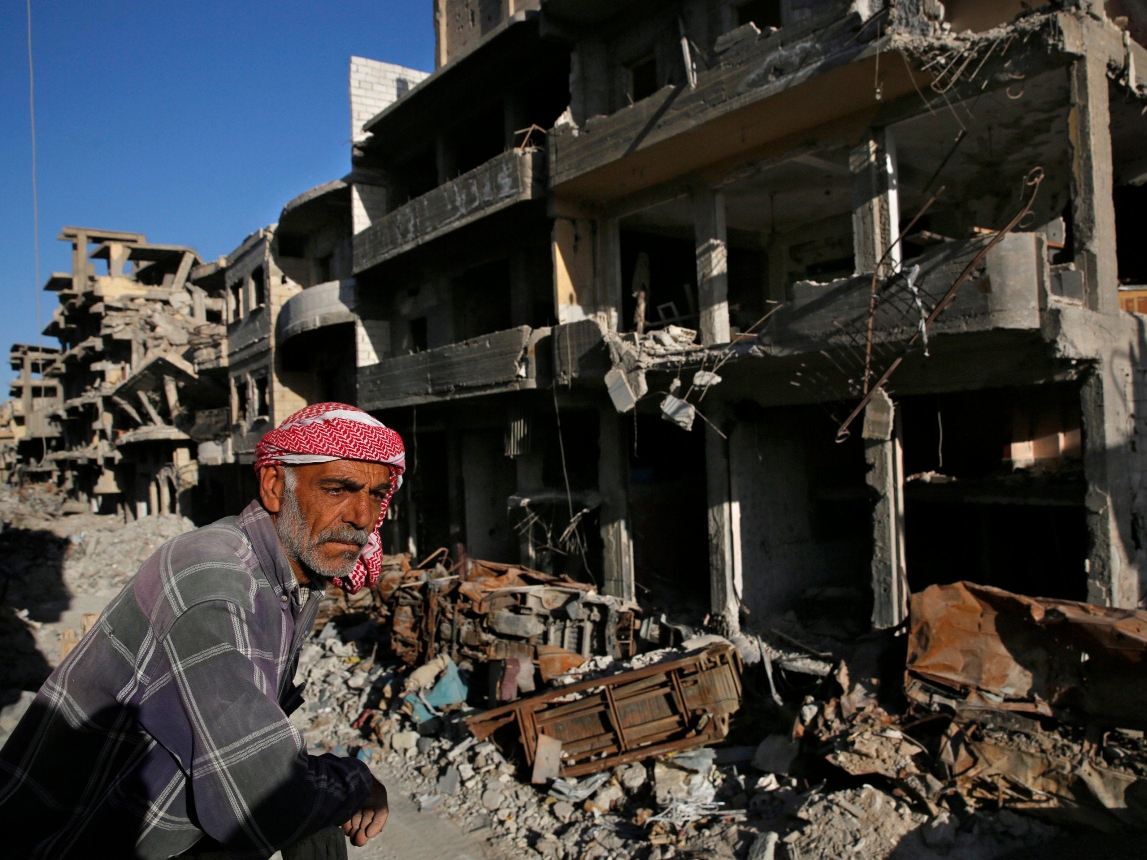 A Syrian man stands between buildings destroyed last summer