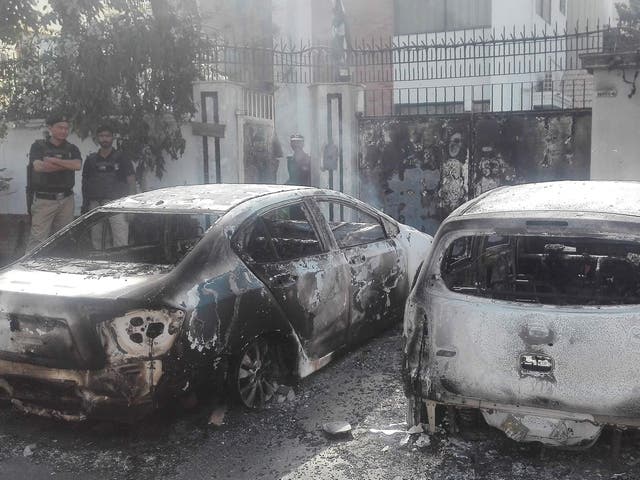 Pakistani security personnel stand next to burned out vehicles in front of the Chinese consulate in Karachi