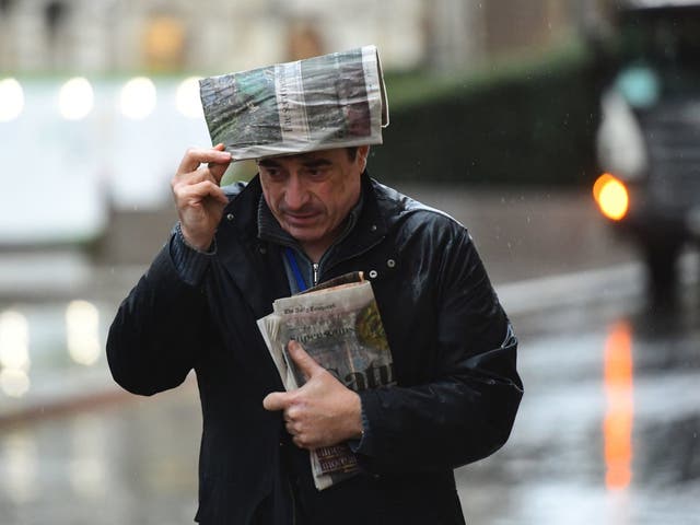 A man takes shelter from the rain beneath a newspaper in London