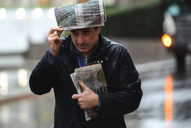 A man takes shelter from the rain beneath a newspaper in London