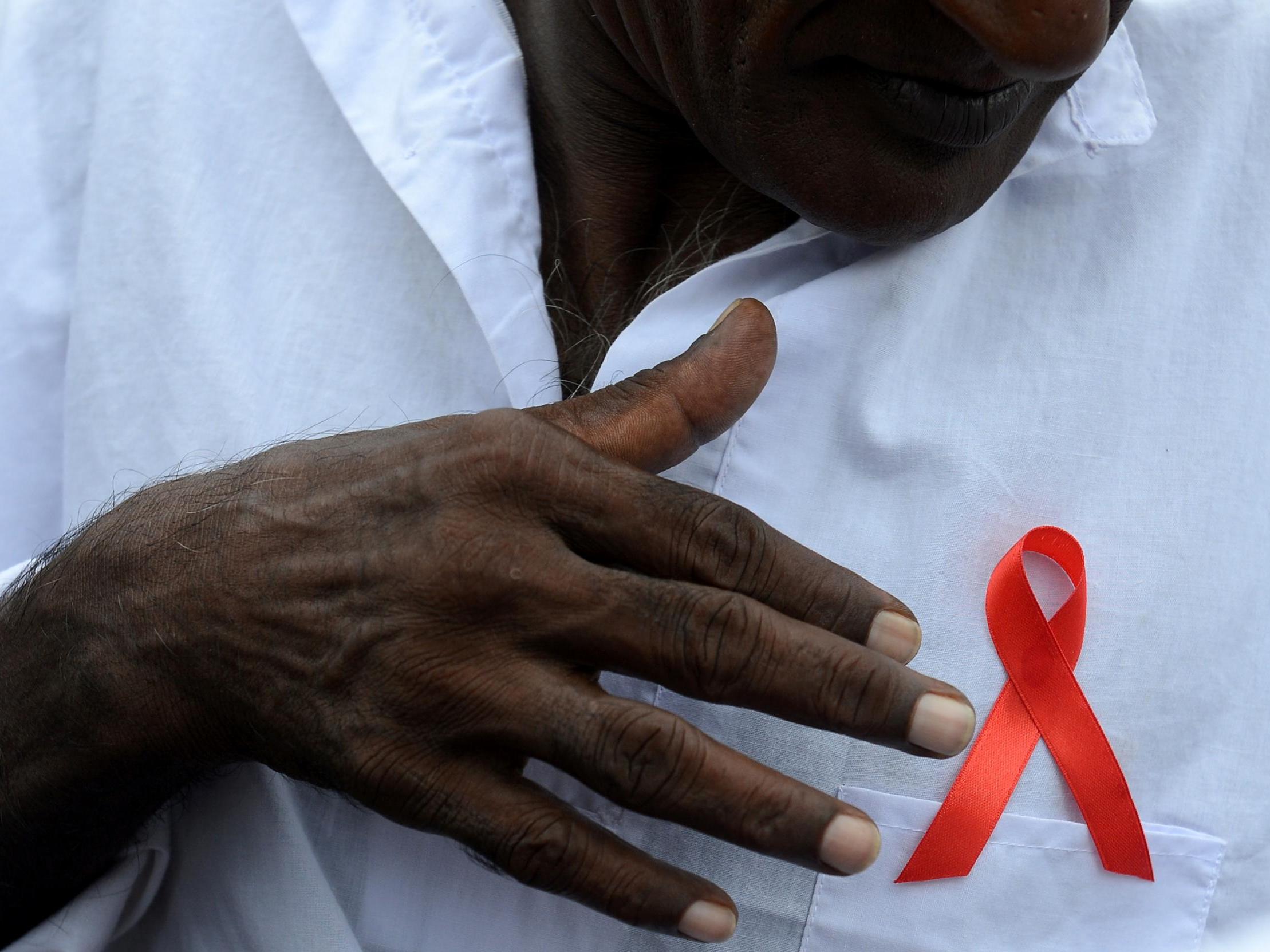 A Sri Lankan man gestures towards a red ribbon on his chest to mark World Aids Day