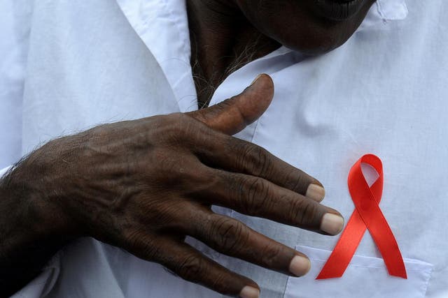 A Sri Lankan man gestures towards a red ribbon on his chest to mark World Aids Day