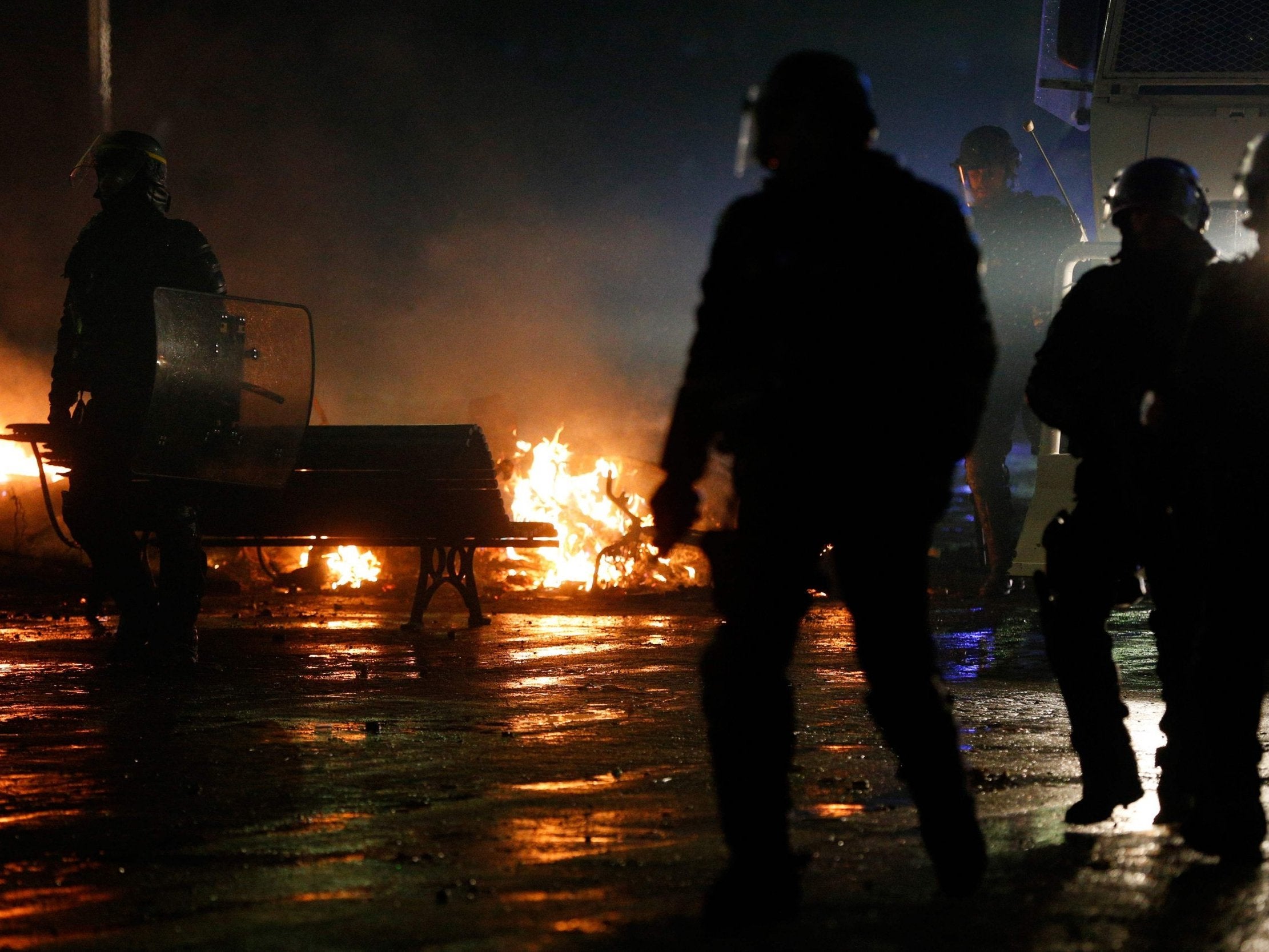Riot police officers walk past a burning barricade amid protests in Paris