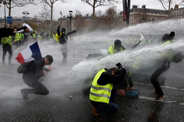 Protesters wearing yellow vests (gilets jaunes) are sprayed with water cannons as they clash with riot police near the Arc de Triomphe