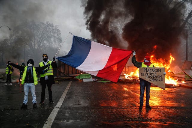 Protesters hold a French flag near a burning barricade during a protest of Yellow vests