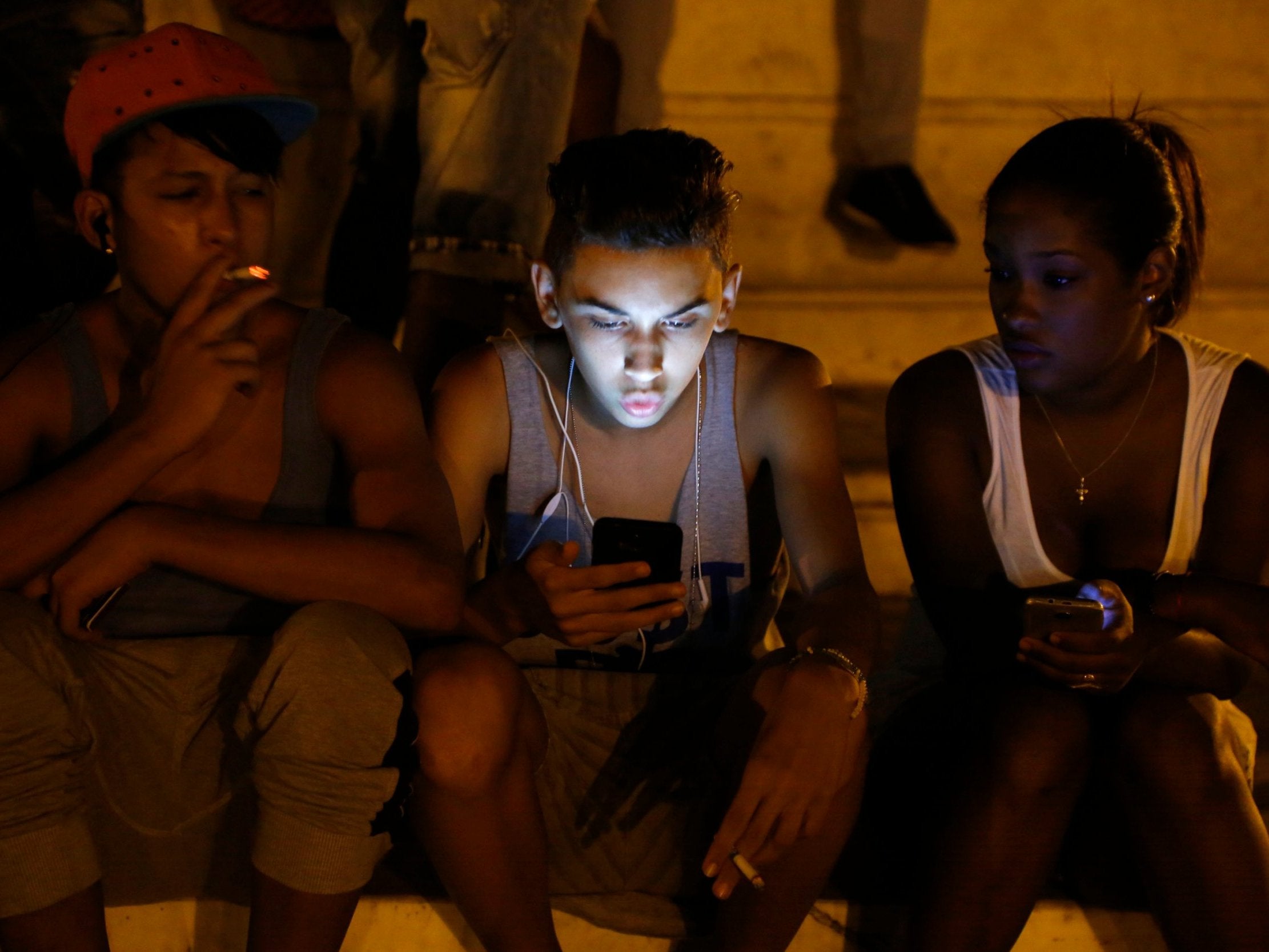 Cuban youths use a password protected wifi network coming from a five star hotel to surf the Internet on their smartphones in downtown Havana