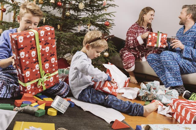 Little boy unwrapping a Christmas gift, parents sitting on couch in background