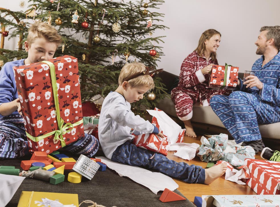 Little boy unwrapping a Christmas gift, parents sitting on couch in background