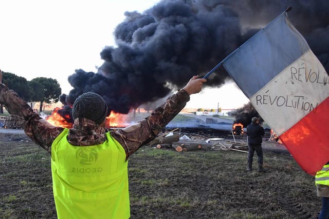 A man wearing a yellow vest waves a French flag in front of burning tyres at a road blockade during a protest against the rise in the price of oil and the cost of living