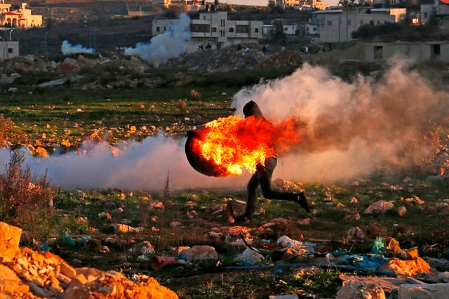 A Palestinian protester on Friday runs with a burning tire during clashes with Israeli troops in Ramallah