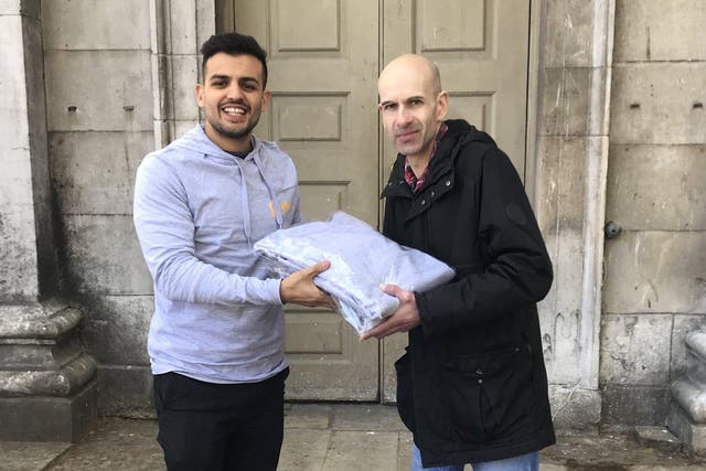 Varun Bhanot, left, the founder of Unhoused.org, gives a donation to a volunteer at the Spitalfields Crypt Trust