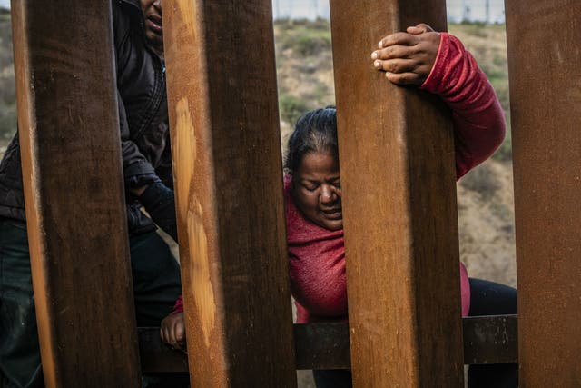 A migrant climbs the border fence before jumping into San Diego, California, from Tijuana, Mexico