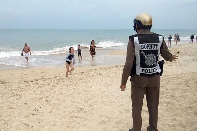 A Thai police officer warns tourists about a swimming ban due to a weather warning at a beach of Koh Samui Island, Surat Thani province