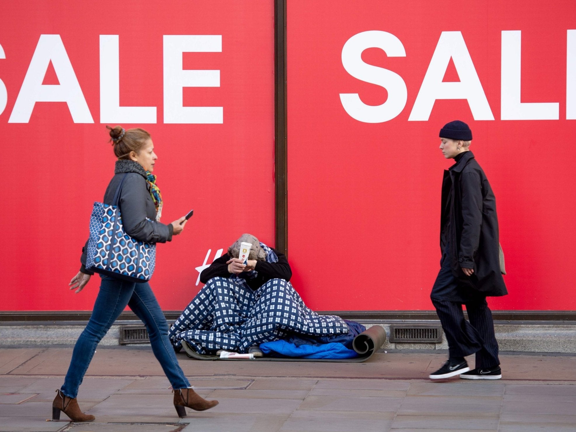 Shoppers walk past a homeless person begging on Oxford Street in central London on 22 December, 2018