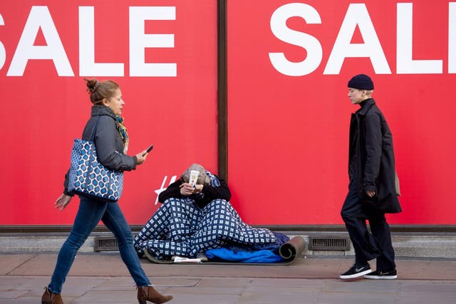 Shoppers walk past a homeless person begging on Oxford Street in central London on 22 December, 2018