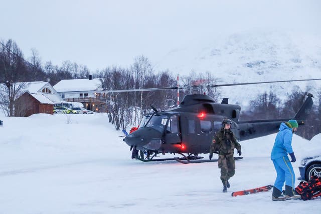 A military helicopter and rescue workers search for the skiers in Tamokdalen, northern Norway