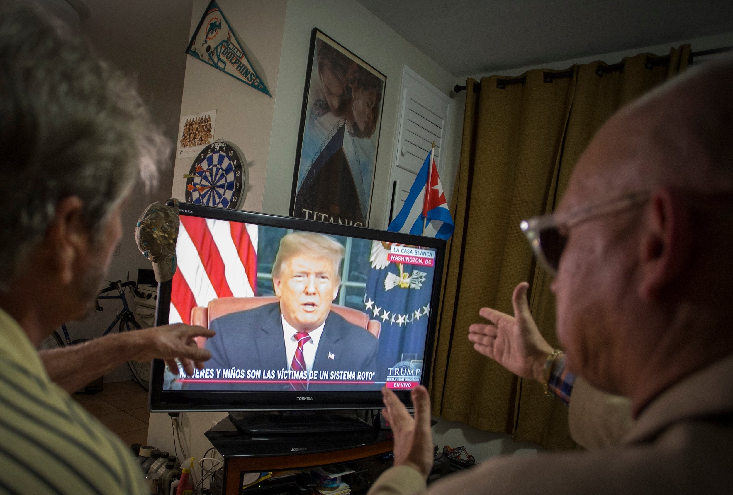 Miguel Saavedra (L) and his friend Oswaldo Hernandez (C) watch President Trump on TV from their home in Miami, Florida