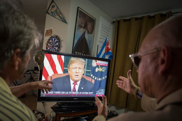Miguel Saavedra (L) and his friend Oswaldo Hernandez (C) watch President Trump on TV from their home in Miami, Florida