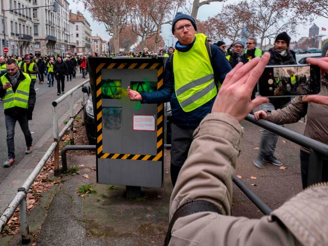 A gilets jaunes protester gives the finger to a vandalised speed camera