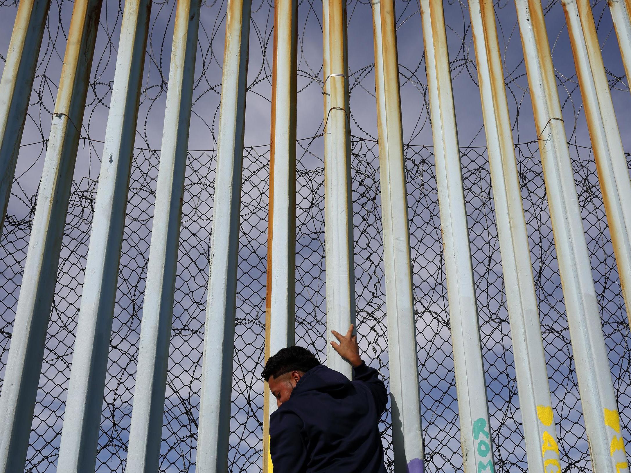 A man holds on to the border wall along the beach in Tijuana, Mexico
