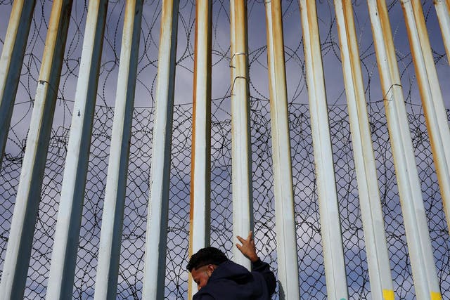 A man holds on to the border wall along the beach in Tijuana, Mexico