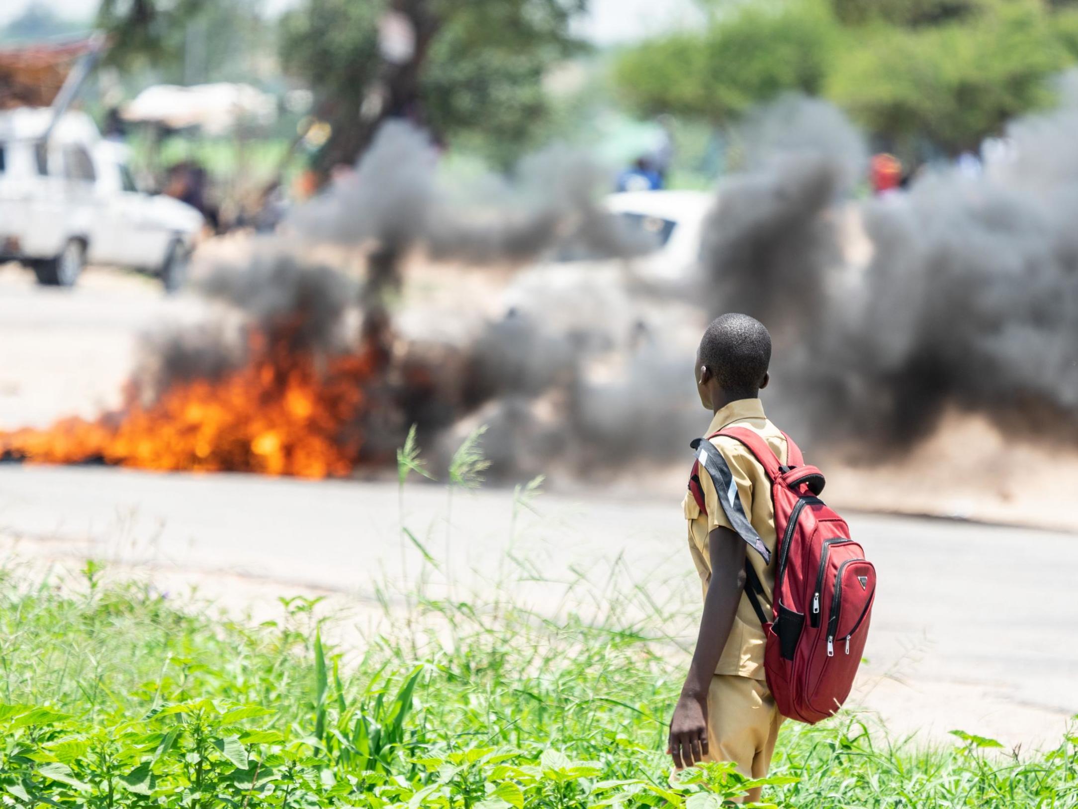 A schoolboy looks at a burning barricade