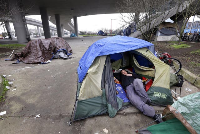 Pictured: A man lies in a tent with others camped nearby, under an overpass in Seattle. Microsoft pledged $500 million to address homelessness and develop affordable housing in response to Seattle widening affordability gap.