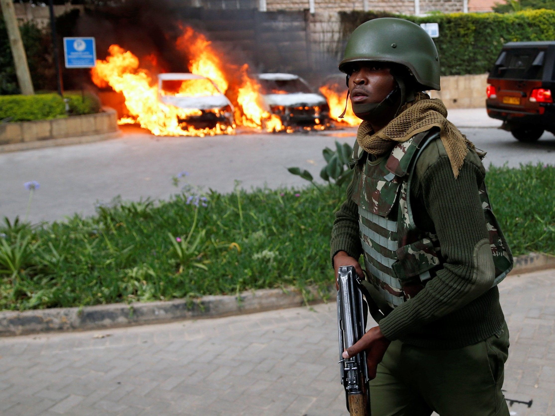 A police officer runs past burning cars at the scene where explosions and gunshots were heard at the Dusit hotel compound in Nairobi