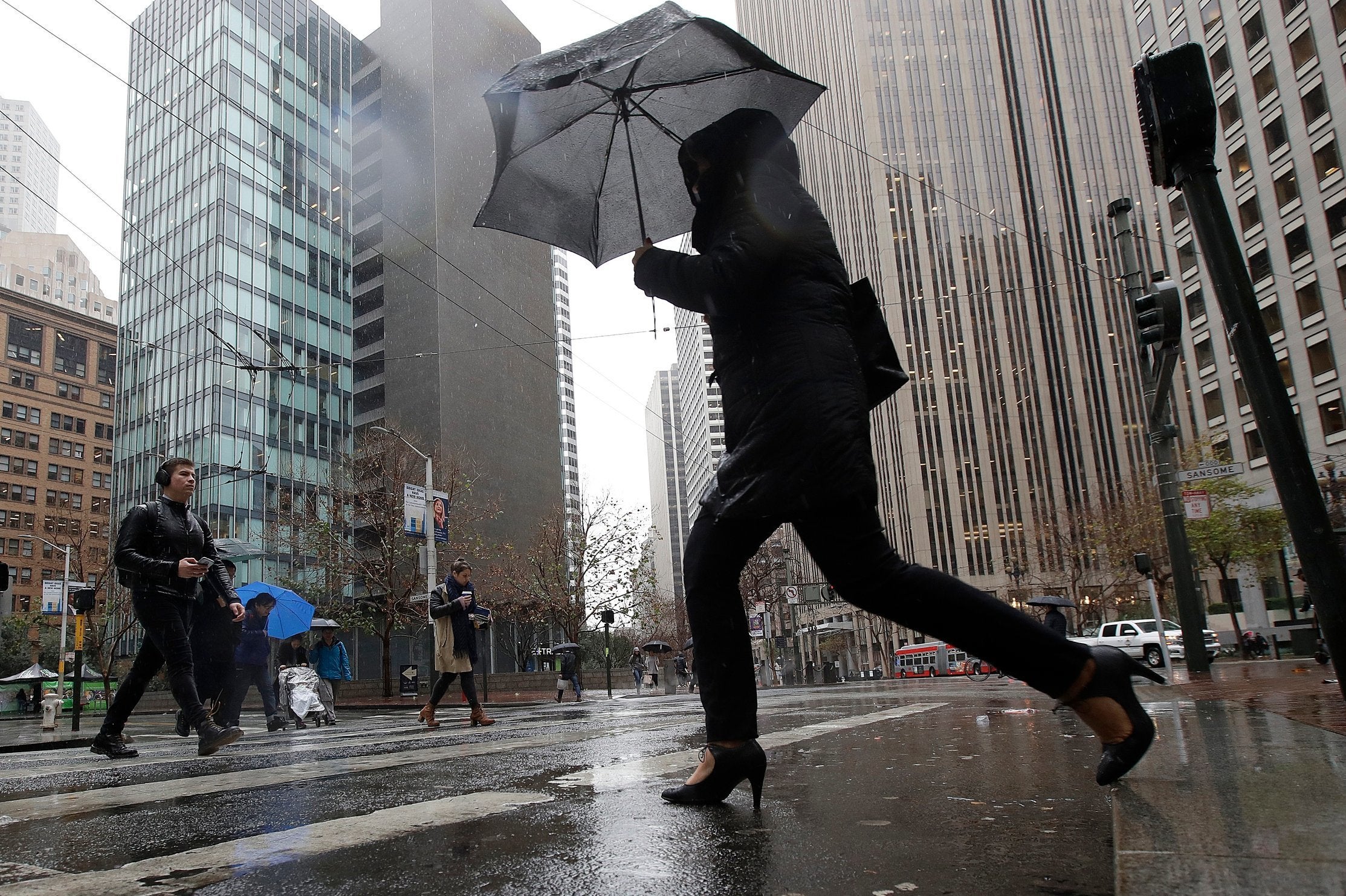 A woman carries an umbrella while crossing a street in San Francisco, Tuesday 15 January 2019. The first in a series of Pacific storms brought rain to much of the state and snow to the mountains.
