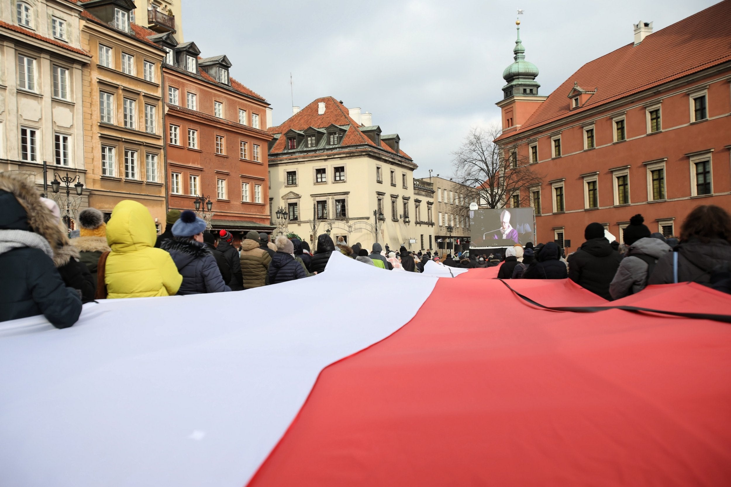 Mourners carry a giant Polish National flag as they gather to watch the funeral service