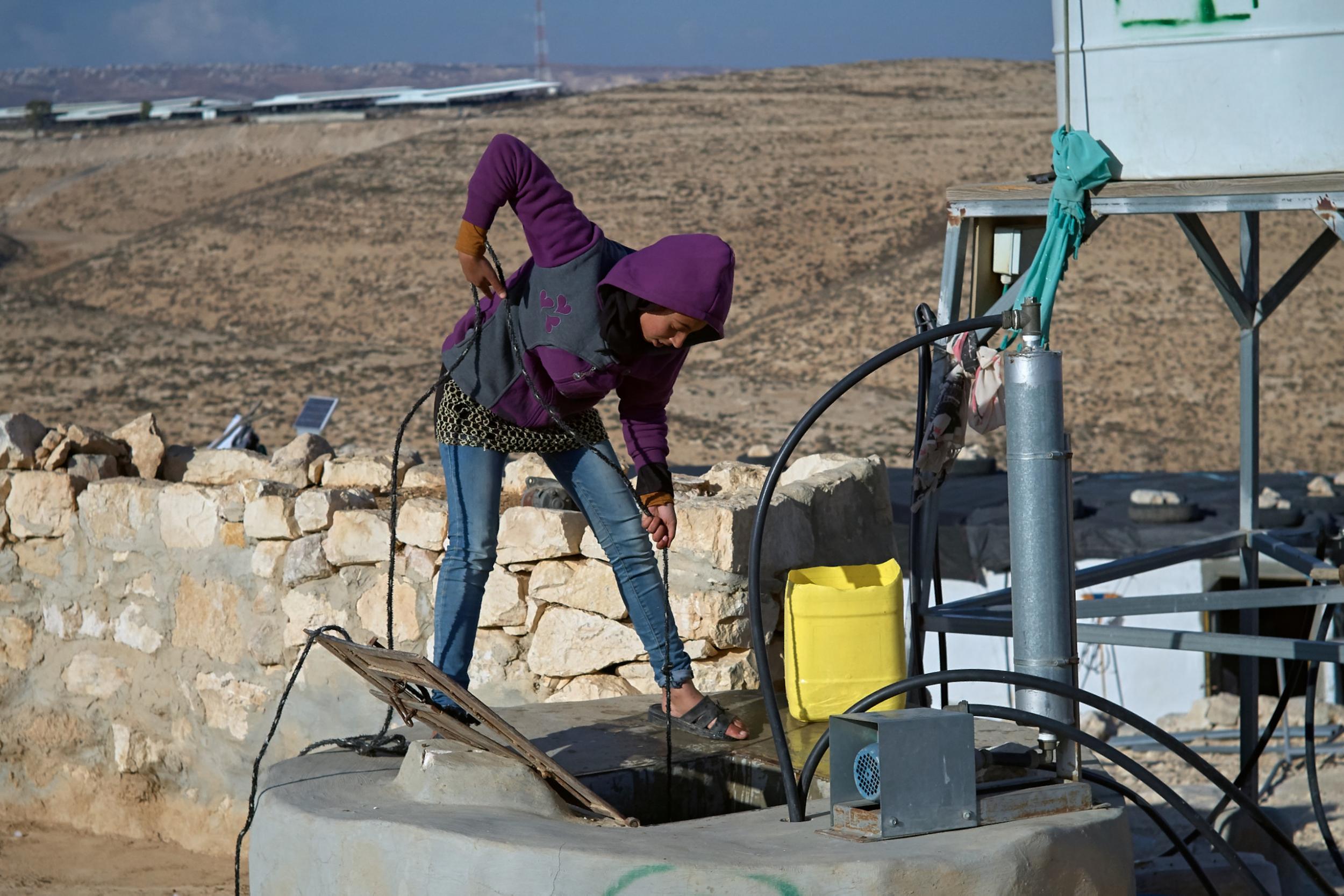 A woman draws water from a well in the Bedouin encampment of Susya – in the background is the Israeli settlement of Susya (Photo: Ben Toren)