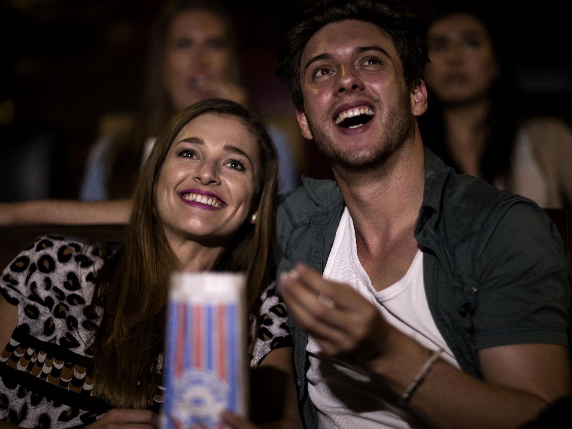 Two young people sitting in a cinema watching a film and eating popcorn