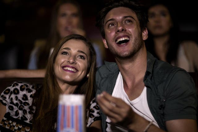 Two young people sitting in a cinema watching a film and eating popcorn